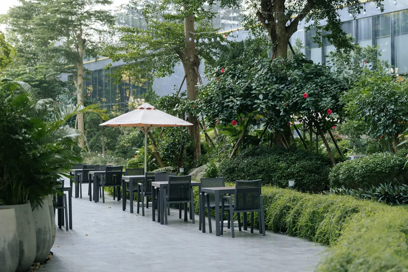 Hiên cà phê ngoài trời với bàn ghế và ô dù giữa vườn cây – Lynntimes Thanh Thủy