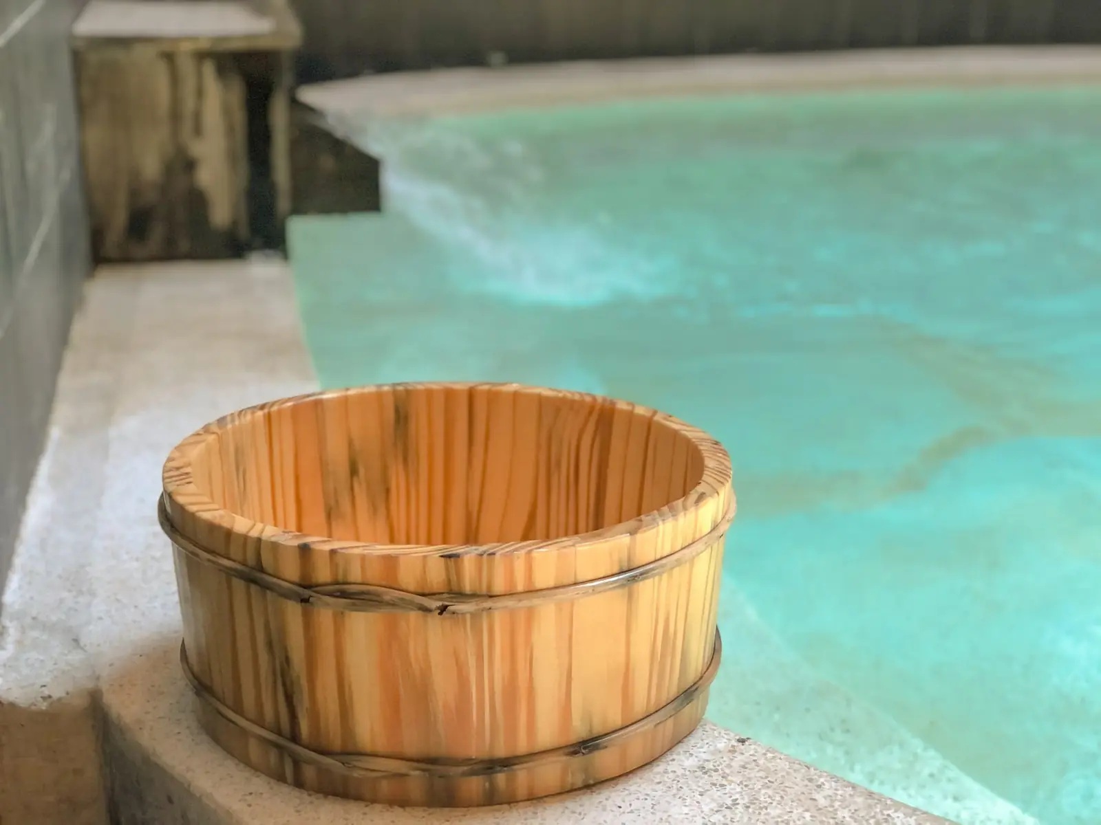 Chậu gỗ truyền thống đặt bên bể khoáng xanh ngọc ở Natural Onsen – Ohayo Onsen & Spa